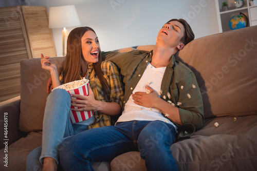 Photo of funny childish lovers dressed casual shirts sitting sofa throwing popcorn sleeping watching movie smiling indoors room home