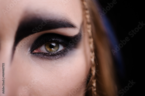 Close-up of eyes with Halloween makeup. Celtic goddess harpy costume smokey eye. Carnival banner. Copy space black background. Magical witch. Macro eyes and make-up.
