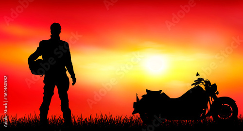 Biker on the background of sunset. Male biker at sunset. Nearby is his motorcycle. Evening, sun, grass