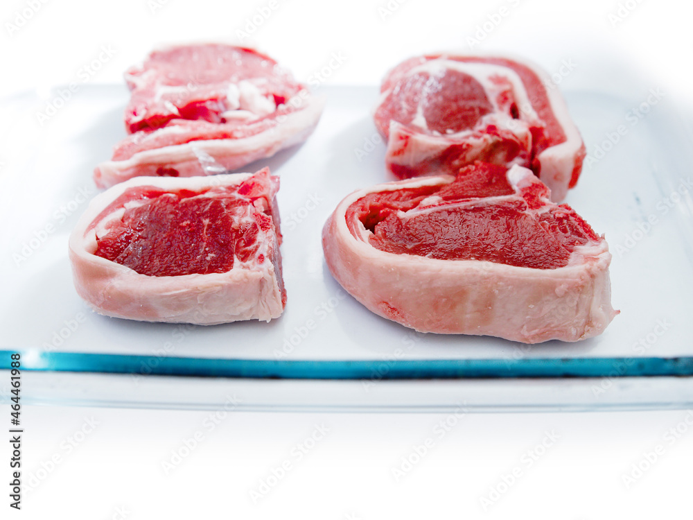 Four fresh uncooked lamb loin chops in a glass tray ready to cook, on white background. Selective focus. Meat industry product. Rich red color of the meat Four fresh uncooked lamb loin chops in a glass tray ready to cook, on white background. Selective focus. Meat industry product. Rich red color of the meat