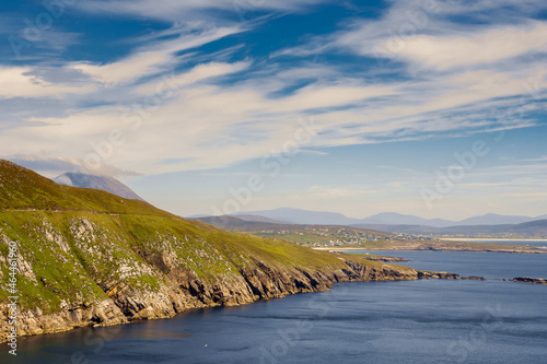 View on amazing Keem bay from a top of a mountain. Warm sunny day. White clouds on blue sky. Spectacular Irish nature landscape. Achill island, Ireland. Nobody. Cliffs and coast line.