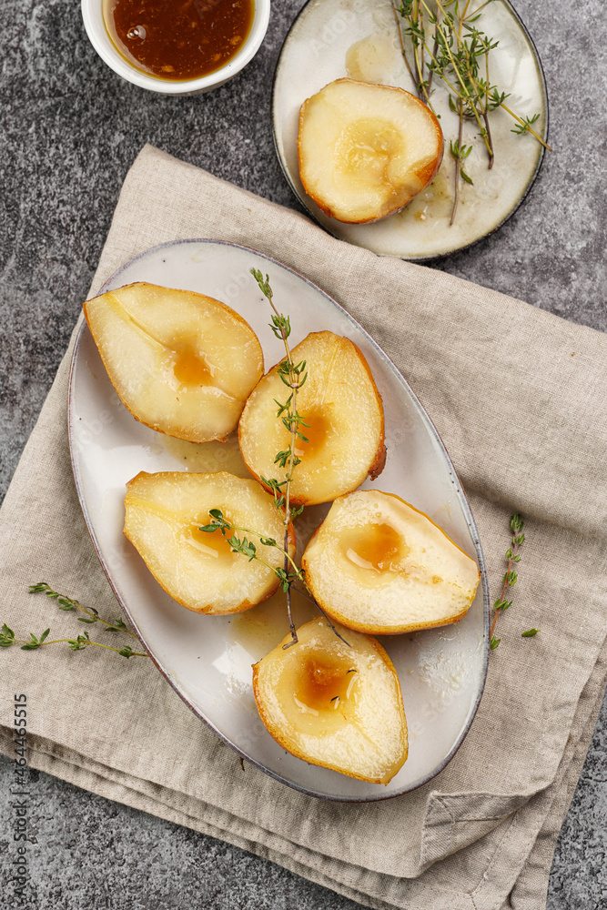 Caramelized pear halves on an oval grey plate with thyme branches and caramel on a linen cloth Caramelized pear halves on an oval grey plate with thyme branches and caramel on a linen cloth