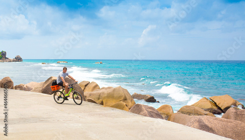 Fototapeta Naklejka Na Ścianę i Meble -  Happy young guy riding a bike on the road by the sea in the Seychelles. Concept of vacation and active lifestyle. Cycling. The man on the bike.