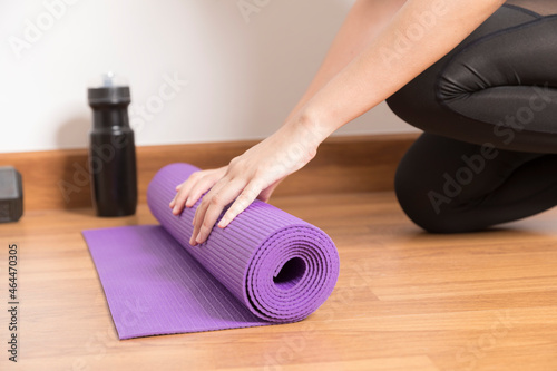 Close-up of woman hands rolling purple yoga mat for playing yoga at home from Covid-19, New normal lifestyle concept.