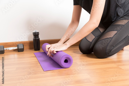 Close-up of woman hands rolling purple yoga mat for playing yoga at home from Covid-19, New normal lifestyle concept.