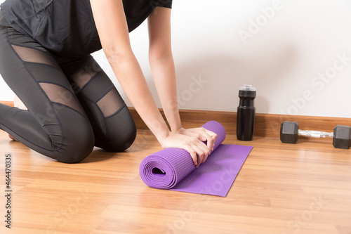 Close-up of woman hands rolling purple yoga mat for playing yoga at home from Covid-19, New normal lifestyle concept.