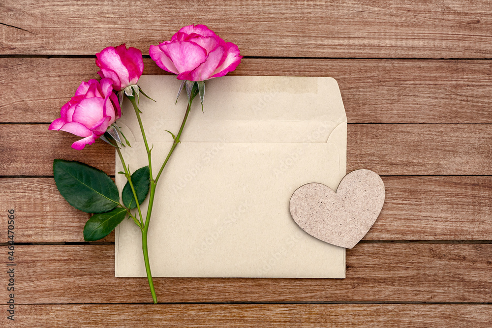 Bouquet of pink roses in an envelope with a heart on a wooden background. Postcard with place for design. Bouquet of pink roses in an envelope with a heart on a wooden background. Postcard with place for design.