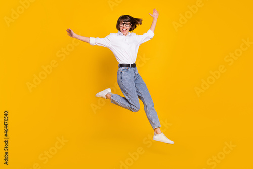 Photo of careless lady jump hurry run wear eyeglasses white shirt jeans shoes isolated yellow color background