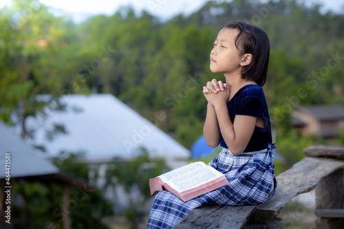 Cute asian little girl read bible and pray in morning with copy space, christian concept.