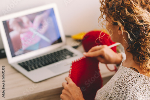 Young woman knitting wool using needle while watching online tutorial on laptop at home. Woman watching needlework lessons on laptop. Caucasian woman learning to knit online. photo
