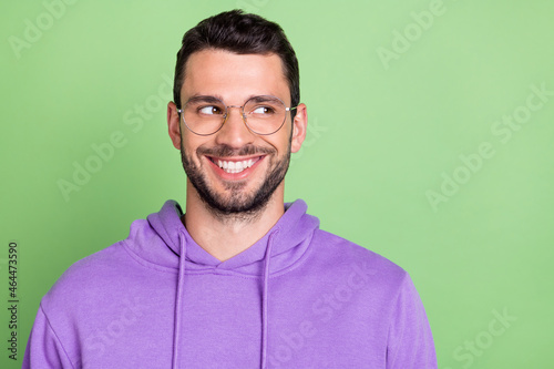 Photo of funny young brunet guy look empty space wear eyewear violet hoodie isolated on green color background © deagreez