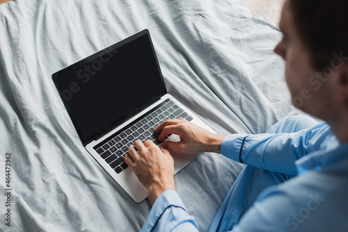 High angle view of blurred man in pajama using laptop with blank screen on bed