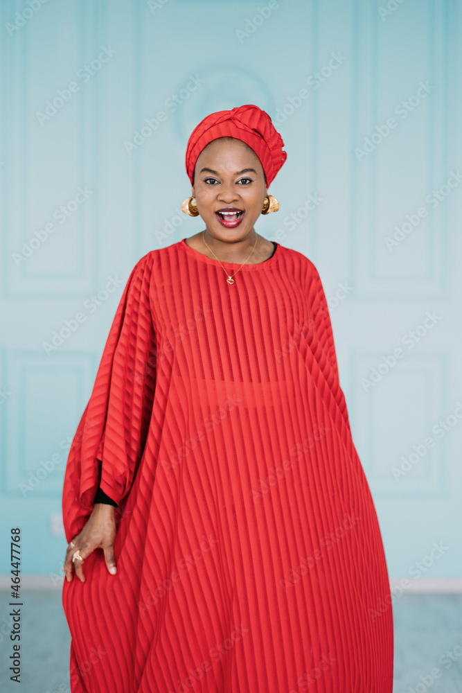 Beautiful positive african american woman wearing red ethnic clothes and headscarf, walking on camera with happy face smiling. Studio shot of pretty lady on blue background Beautiful positive african american woman wearing red ethnic clothes and headscarf, walking on camera with happy face smiling. Studio shot of pretty lady on blue background