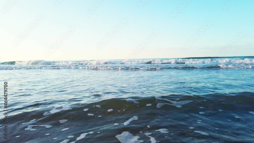 Low angle wide slow motion of waves rolling on a beach in autumnal light