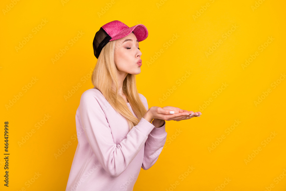 Photo of pretty flirty young lady wear pink sweater headwear sending kiss arms empty space isolated yellow color background