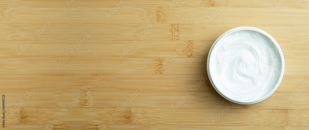 Cosmetic cream banner background. White cosmetic cream for skin and body in an open white jar on a wooden bamboo empty background. Copy space Cosmetic cream banner background. White cosmetic cream for skin and body in an open white jar on a wooden bamboo empty background. Copy space