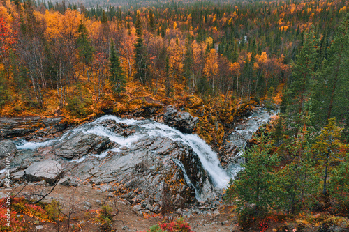Beautiful mountain waterfall among rocks and trees. View of the autumn colorful forest and tundra in the Arctic,Kola Peninsula. Autumn arctic landscape. Austere, cold atmosphere. 