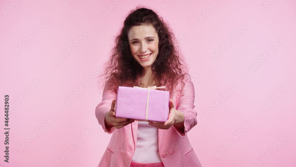 brunette and happy young woman looking at camera while holding present isolated on pink brunette and happy young woman looking at camera while holding present isolated on pink
