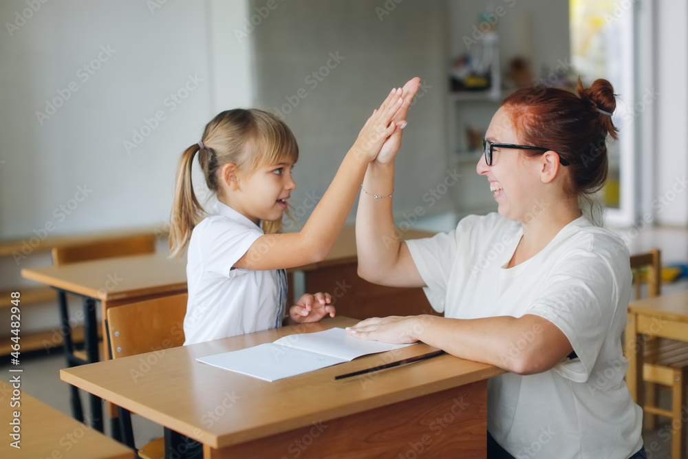 The teacher deals with the child with the girl, the teacher helps explain to the child in the classroom at the desk. Educational school process, bright room and the joy of learning