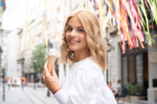 A beautiful teenage girl smiles on the colorful street with an ice cream cone in her hand.
