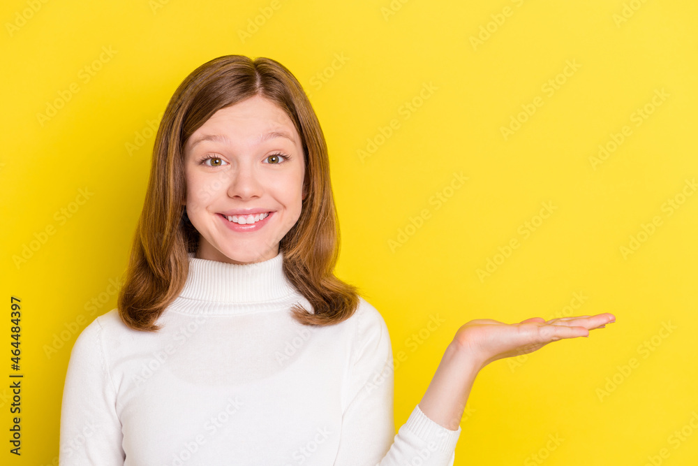 Photo of attractive nice small girl hold hand empty space object offer smile isolated on yellow color background Photo of attractive nice small girl hold hand empty space object offer smile isolated on yellow color background
