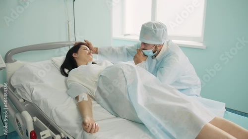 Pregnant woman with painful contractions holding hand of her caring husband that sitting near at hospital ward. Young couple preparing for birth of their child photo