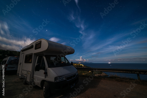 Night sky at Monte Argentario peninsula, Tuscany, Italy. Stars over camper van illuminated by moon light. Giglio Island in the background.