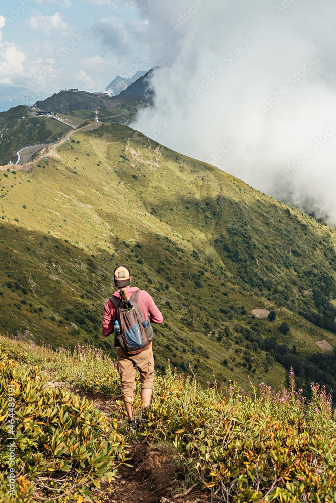 Young man with backpack hiking in the Caucasus green mountains among the bushes of rhododendron , active and healthy lifestyle, landscape Young man with backpack hiking in the Caucasus green mountains among the bushes of rhododendron , active and healthy lifestyle, landscape