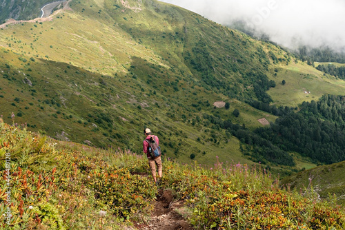 Young man with a backpack walking in the Caucasus green mountains among the bushes of rhododendron , active and healthy lifestyle, landscape © Lena_viridis