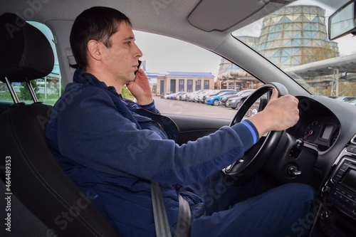 A man is driving in a car and talking on the phone against the background of an industrial enterprise