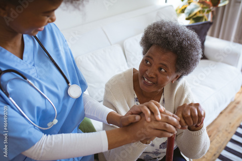 Smiling african american female doctor holding hands of senior female patient at home