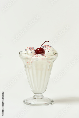 Vanilla sundae ice cream in cup with sweet grains and bing cherry on top isolated on white background