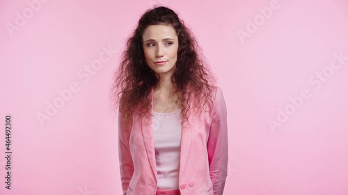 brunette and curly young woman looking away isolated on pink