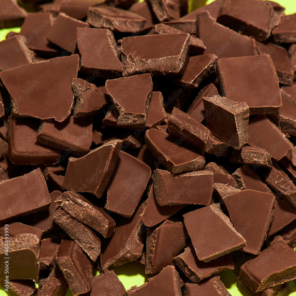 Closeup of broken, crushed dark chocolate bars stack isolated over green background