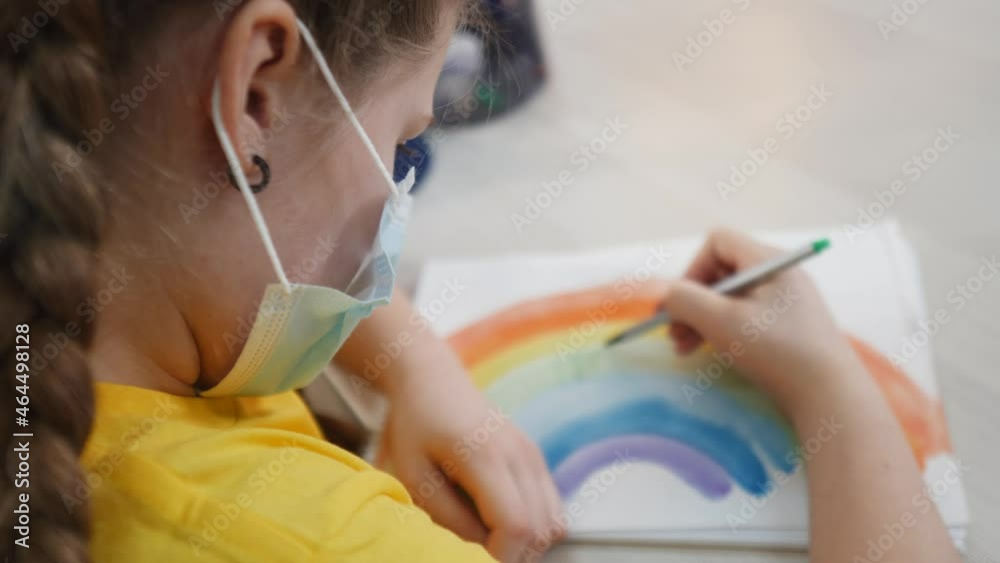 child kid in a mask draws a rainbow at home. stay at home coronavirus concept. girl kid in protective mask draws a rainbow fun at kindergarten. Kid rainbow drawing coronavirus. stay home child kid in a mask draws a rainbow at home. stay at home coronavirus concept. girl kid in protective mask draws a rainbow fun at kindergarten. Kid rainbow drawing coronavirus. stay home