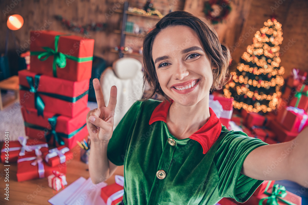 Photo of influencer lady make selfie show fingers v-sign wear elf costume in decorated office indoors Photo of influencer lady make selfie show fingers v-sign wear elf costume in decorated office indoors