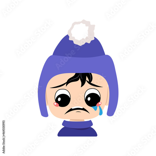 Baby with crying and tears emotion, sad face, depressive eyes in blue hat with pompom. Kid with melancholy expression in autumnal or winter headdress