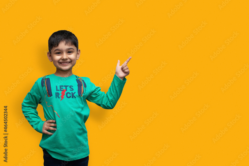 Happy young boy in shirt pointing up and holding arm white looking at the camera over isolated background and copy space