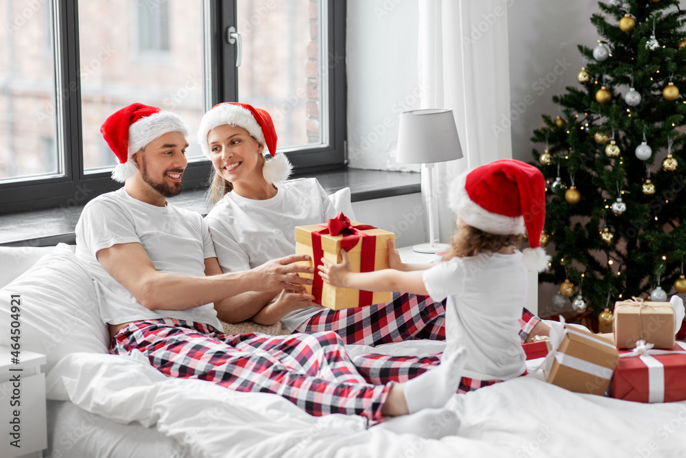 Fototapeta premium family, winter holidays and people concept - happy mother, father and little daughter with christmas gifts in bed at home