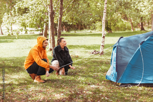 camping, tourism and travel concept - happy couple setting up tent outdoors