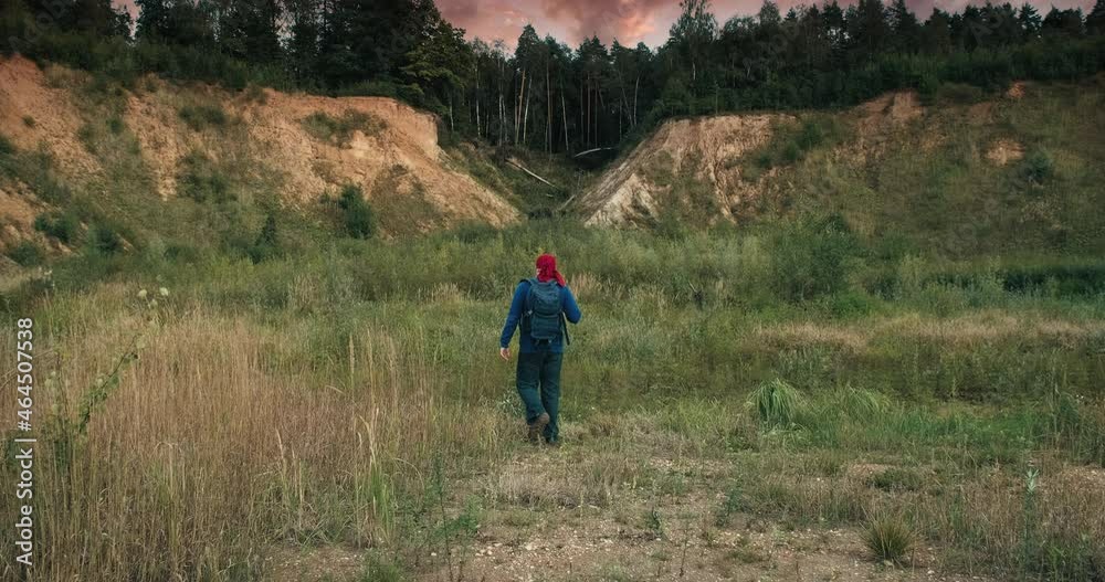 Hiker walks with a backpack in a large, sandy quarry at sunset. The quarry is overgrown with grass and trees. The concept of hiking a healthy lifestyle and weekends in the fresh air Hiker walks with a backpack in a large, sandy quarry at sunset. The quarry is overgrown with grass and trees. The concept of hiking a healthy lifestyle and weekends in the fresh air