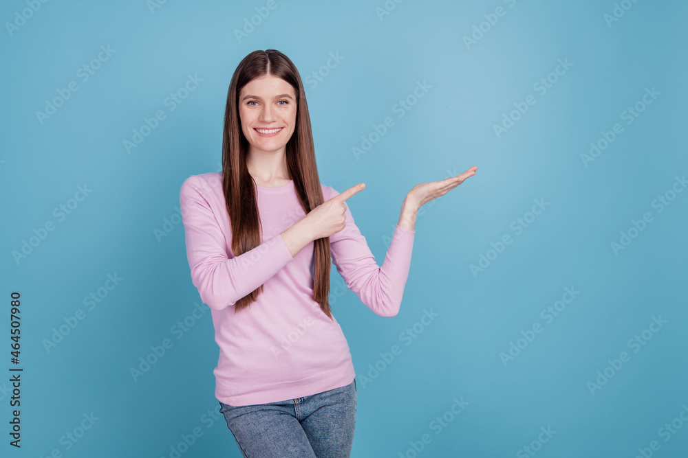Photo of young girl happy positive smile point finger product promo offer sale isolated on blue color background Photo of young girl happy positive smile point finger product promo offer sale isolated on blue color background