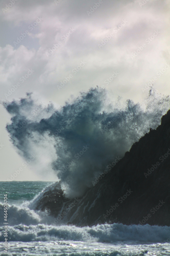 Beautiful foamy ocean wave crashing on a rough coastal rock, vertical wallpaper
