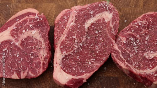 Seasoning raw ribeye beef steaks with rosemary