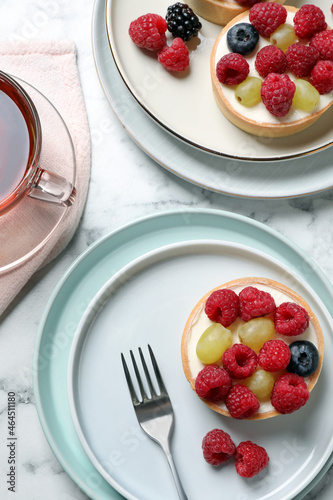 Delicious tartlets with berries and tea on white marble table, flat lay