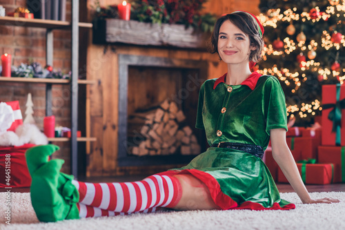 Photo of funny sweet young woman dressed green costume smiling celebrating new year sitting floor indoors room home house
