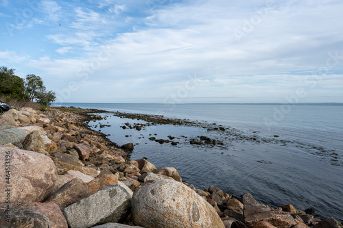 A rocky shoreline with blue water and a blu sky in the background. Picture from Skalderviken, southern Sweden