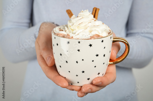 Woman holding cup of delicious hot chocolate with whipped cream and cinnamon sticks, closeup