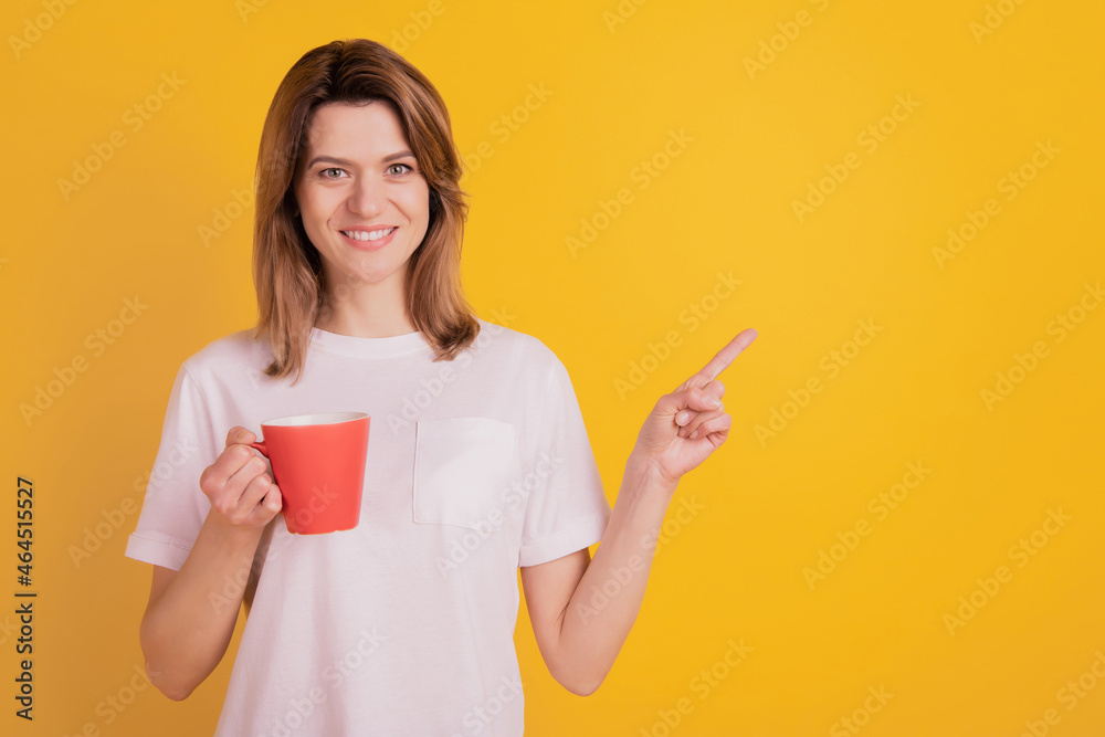 Photo of promoter lady hold red cup drink tea direct finger empty space wear casual t-shirt on yellow background Photo of promoter lady hold red cup drink tea direct finger empty space wear casual t-shirt on yellow background
