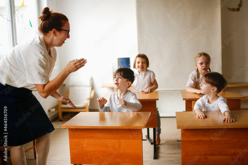 teacher with children in class beats rhythm on desks, teacher helps explain the lesson to the children in class dynamic game. Educational school process, bright room and interesting learning